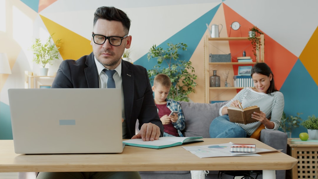 Man working on laptop while family relaxes in background